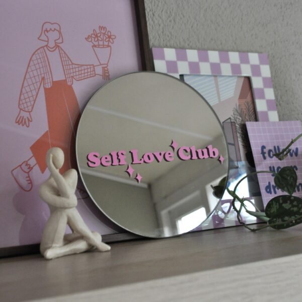 Ronde spiegel op een plank met de tekst 'self love club' in roze vinyl