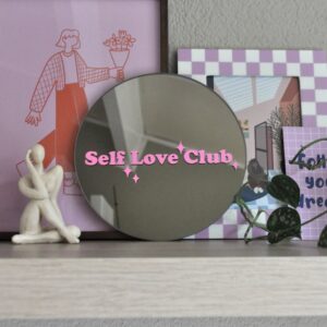 Ronde spiegel op een plank met de tekst 'self love club' in roze vinyl