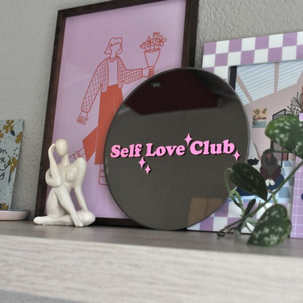 Ronde spiegel op een plank met de tekst 'self love club' in roze vinyl